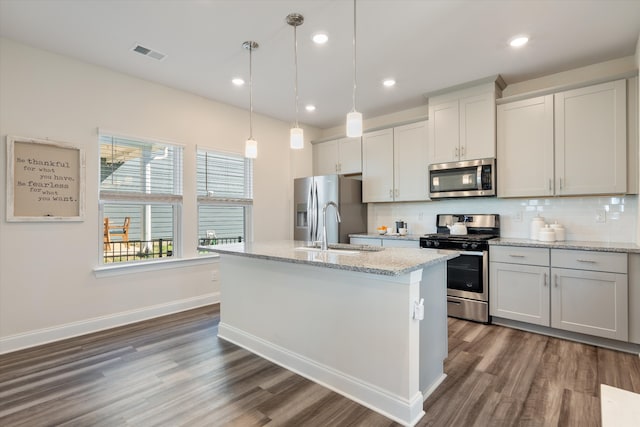 kitchen featuring dark wood-type flooring, hanging light fixtures, an island with sink, and appliances with stainless steel finishes