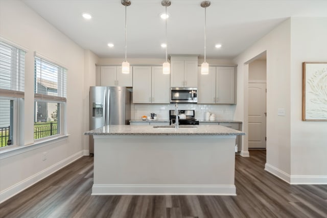 kitchen with a kitchen island with sink, appliances with stainless steel finishes, hanging light fixtures, and sink