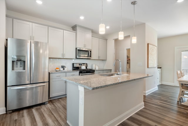 kitchen featuring a center island with sink, sink, light stone counters, hanging light fixtures, and appliances with stainless steel finishes