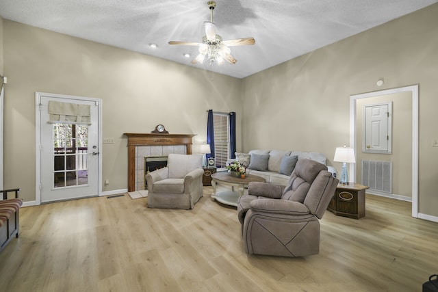 living room featuring ceiling fan, a textured ceiling, light hardwood / wood-style floors, and a tile fireplace