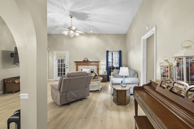 living room with a fireplace, light hardwood / wood-style flooring, a textured ceiling, and ceiling fan