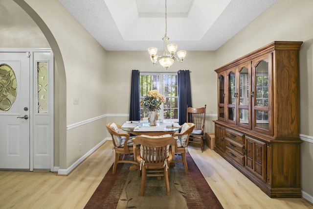 dining area with a raised ceiling, a notable chandelier, light wood-type flooring, and a textured ceiling