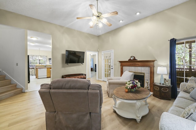 living room with ceiling fan, a textured ceiling, light hardwood / wood-style flooring, a high ceiling, and a fireplace