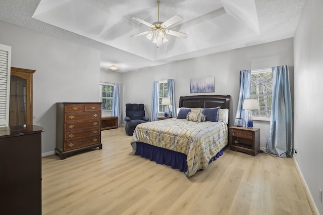 bedroom featuring ceiling fan, a textured ceiling, light wood-type flooring, and a raised ceiling