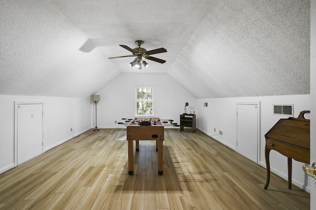 recreation room featuring ceiling fan, a textured ceiling, light hardwood / wood-style flooring, and lofted ceiling