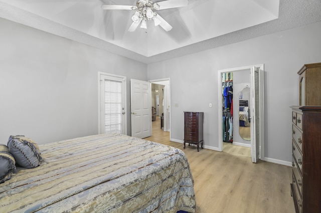 bedroom featuring a walk in closet, ceiling fan, light hardwood / wood-style flooring, a raised ceiling, and a closet