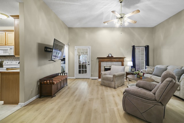 living room with a fireplace, light hardwood / wood-style flooring, a textured ceiling, and ceiling fan