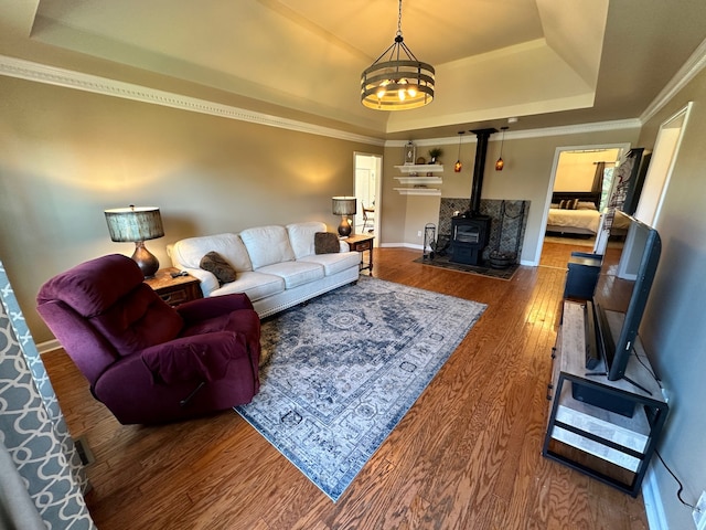 living room with a wood stove, hardwood / wood-style flooring, a tray ceiling, an inviting chandelier, and ornamental molding