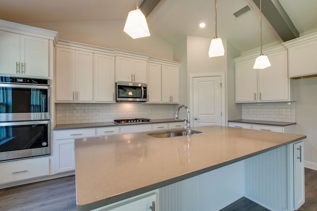 kitchen featuring a center island with sink, sink, hanging light fixtures, vaulted ceiling with beams, and stainless steel appliances