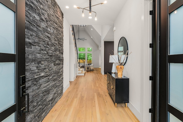 hall featuring light wood-type flooring, a chandelier, and high vaulted ceiling