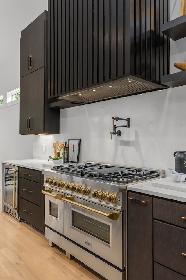 kitchen with wine cooler, dark brown cabinets, backsplash, double oven range, and light wood-type flooring