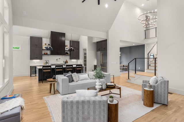 living room with an inviting chandelier, light wood-type flooring, sink, and high vaulted ceiling