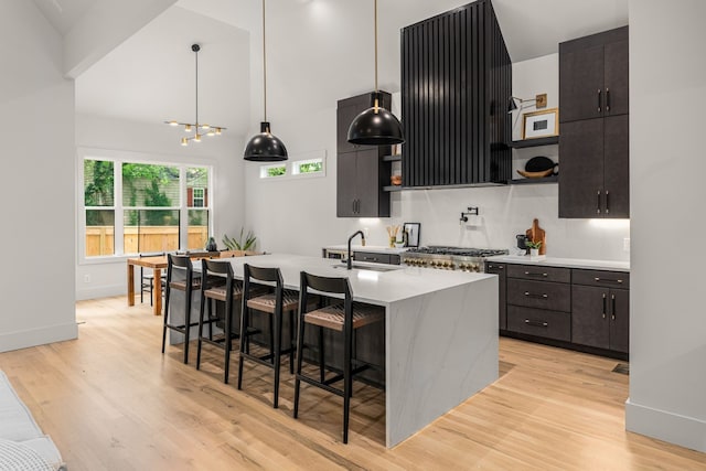 kitchen featuring light hardwood / wood-style floors, a kitchen island with sink, a breakfast bar area, sink, and hanging light fixtures