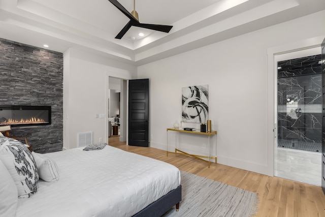 bedroom featuring ceiling fan, hardwood / wood-style flooring, a tray ceiling, and a fireplace