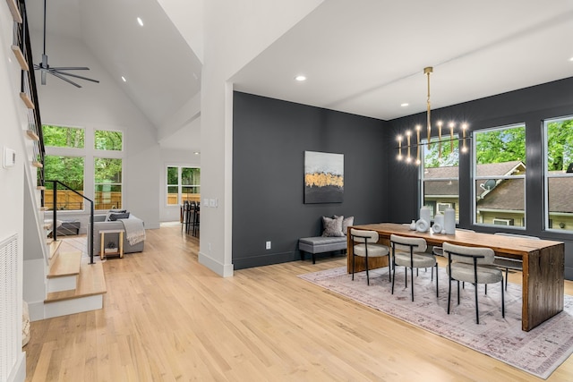 dining space featuring ceiling fan with notable chandelier, high vaulted ceiling, and light hardwood / wood-style flooring