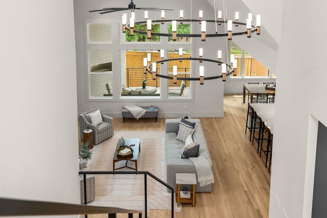 living room with ceiling fan with notable chandelier, light hardwood / wood-style floors, and a high ceiling