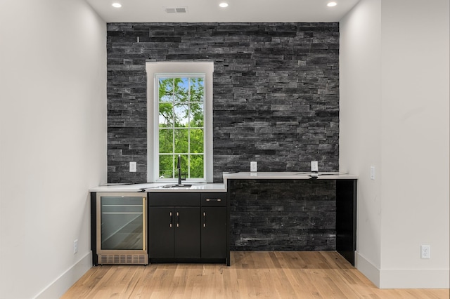 bar featuring beverage cooler, sink, and light hardwood / wood-style floors