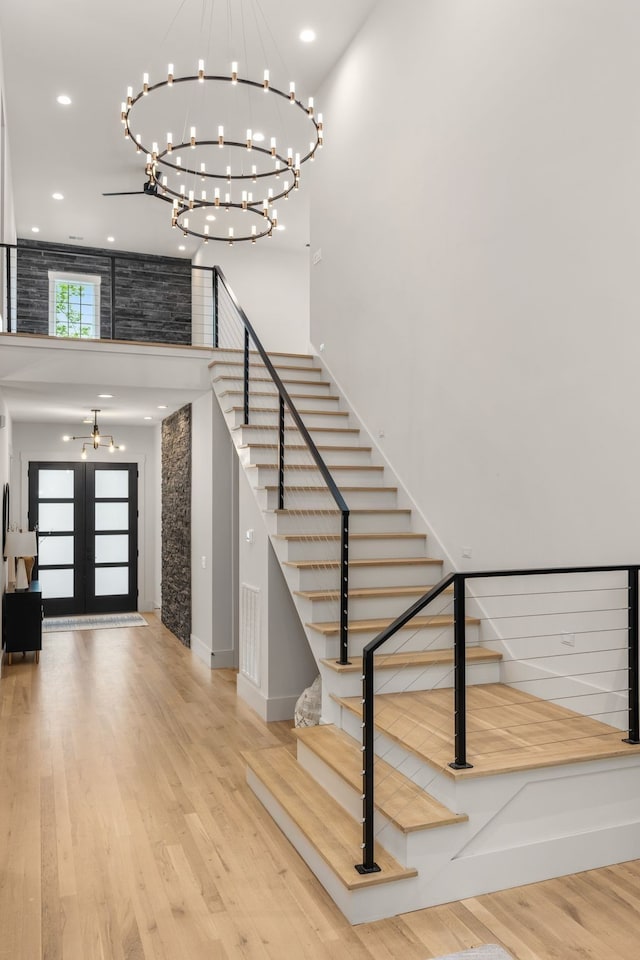 foyer entrance with a towering ceiling, a notable chandelier, french doors, and hardwood / wood-style flooring