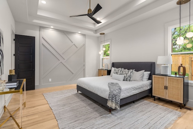 bedroom featuring light hardwood / wood-style floors, a tray ceiling, and ceiling fan