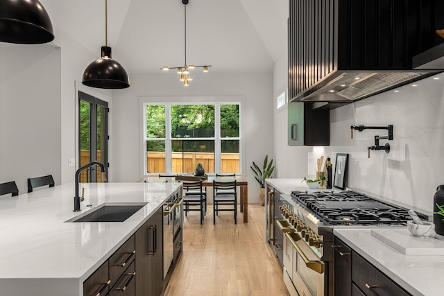 kitchen featuring range with two ovens, wall chimney range hood, pendant lighting, sink, and light stone counters