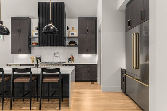 kitchen with built in refrigerator, ventilation hood, a breakfast bar area, light hardwood / wood-style flooring, and dark brown cabinetry