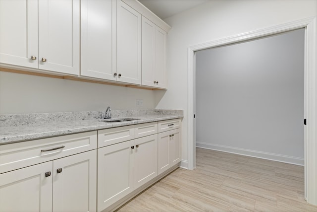 kitchen with light stone counters, white cabinets, light wood-type flooring, and sink