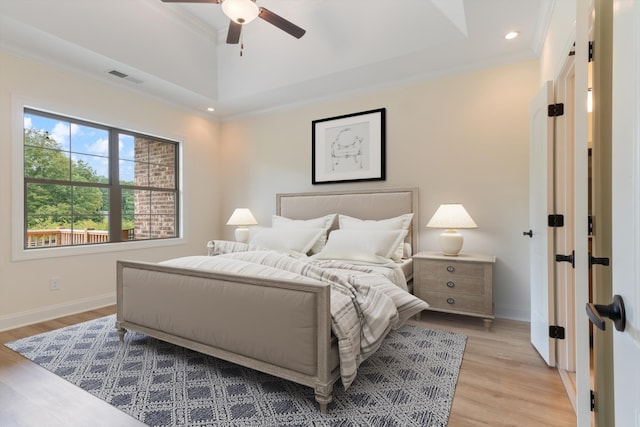 bedroom featuring ornamental molding, light wood-type flooring, ceiling fan, and a tray ceiling