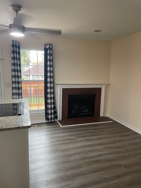 unfurnished living room featuring a brick fireplace, dark hardwood / wood-style floors, and ceiling fan