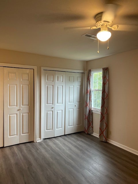 unfurnished bedroom featuring ceiling fan, dark wood-type flooring, and multiple closets