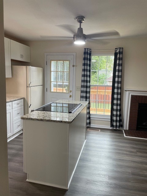 kitchen with black electric stovetop, a kitchen island, plenty of natural light, and white cabinetry