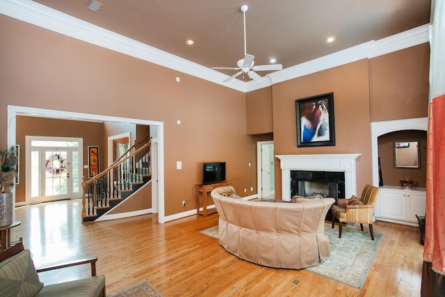 living room with crown molding, ceiling fan, a towering ceiling, and light hardwood / wood-style floors