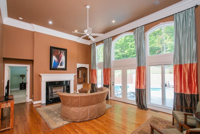 living room featuring ceiling fan, french doors, wood-type flooring, a fireplace, and crown molding