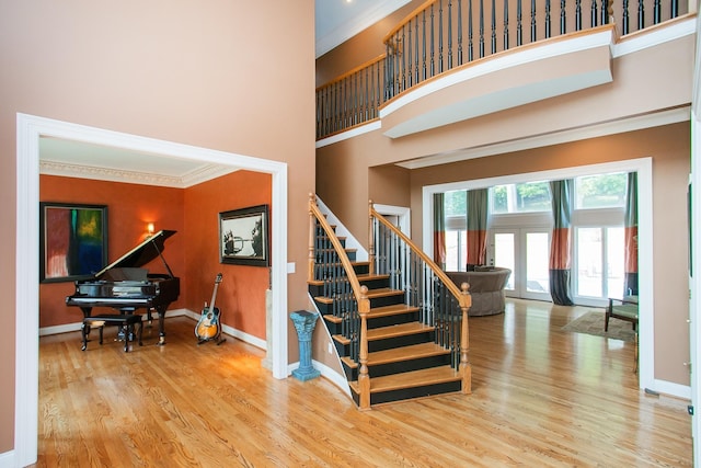 staircase featuring french doors, hardwood / wood-style flooring, a towering ceiling, and crown molding