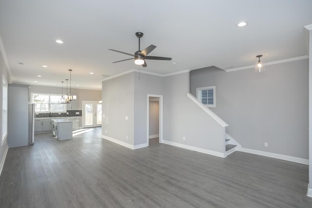 unfurnished living room with ceiling fan with notable chandelier, crown molding, and dark wood-type flooring