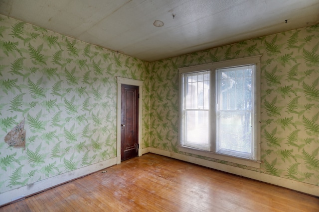 unfurnished room featuring wood finished floors, baseboards, and wallpapered walls