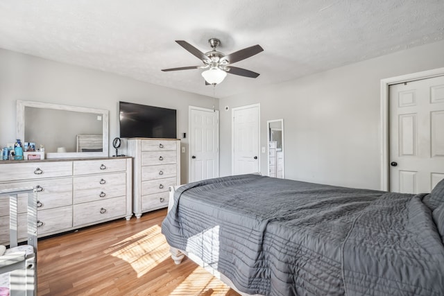 bedroom featuring a textured ceiling, ceiling fan, multiple closets, and light hardwood / wood-style flooring