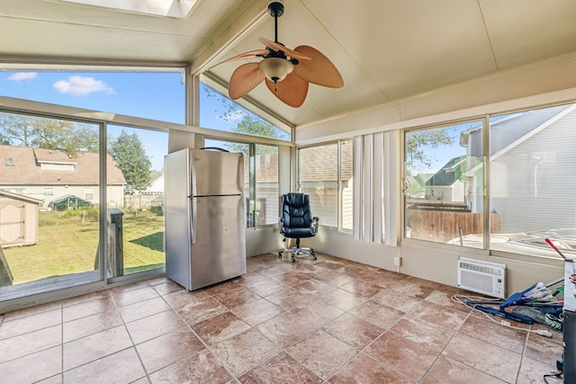 unfurnished sunroom featuring ceiling fan, a wall mounted AC, lofted ceiling with skylight, and a wealth of natural light