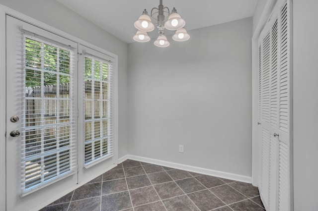 unfurnished dining area with dark tile patterned floors and an inviting chandelier