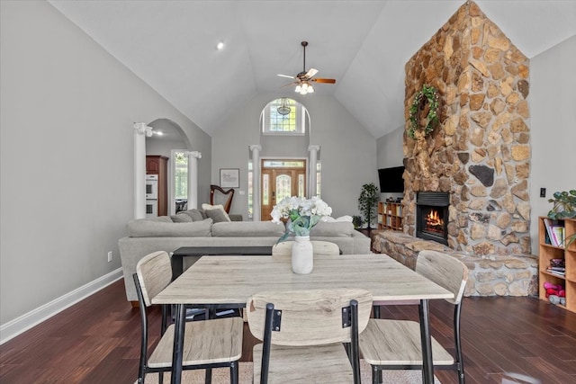 dining area with ceiling fan, a stone fireplace, dark hardwood / wood-style flooring, and high vaulted ceiling