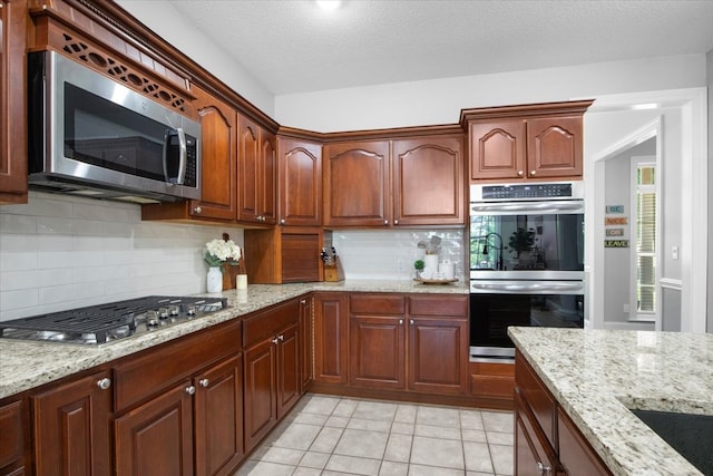 kitchen with light stone counters, a textured ceiling, decorative backsplash, light tile patterned floors, and appliances with stainless steel finishes