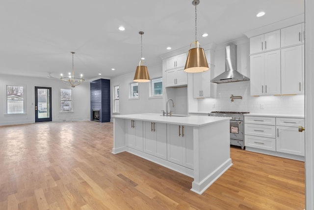 kitchen with wall chimney exhaust hood, high end stove, a kitchen island with sink, sink, and white cabinetry