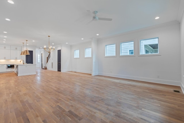 unfurnished living room with sink, light hardwood / wood-style floors, ceiling fan with notable chandelier, and ornamental molding