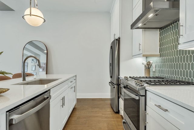 kitchen with white cabinets, decorative light fixtures, wall chimney exhaust hood, light hardwood / wood-style flooring, and appliances with stainless steel finishes