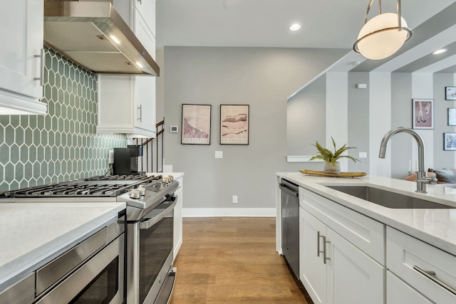 kitchen with stainless steel appliances, sink, wall chimney range hood, white cabinetry, and hanging light fixtures