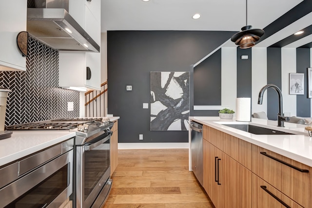 kitchen with wall chimney exhaust hood, light hardwood / wood-style floors, stainless steel appliances, sink, and decorative backsplash