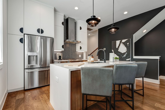 kitchen with wall chimney range hood, a kitchen island with sink, light wood-type flooring, sink, and appliances with stainless steel finishes