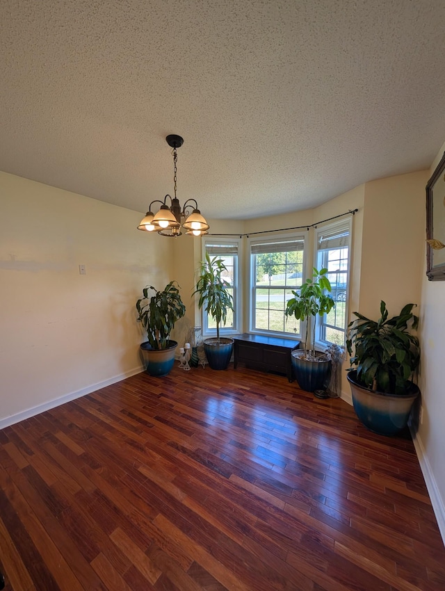 unfurnished dining area with a chandelier, a textured ceiling, baseboards, and wood finished floors