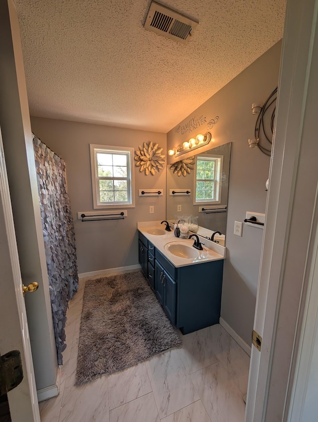 full bath with a sink, visible vents, double vanity, and a textured ceiling