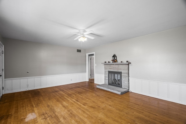 unfurnished living room with a stone fireplace, wood-type flooring, and ceiling fan