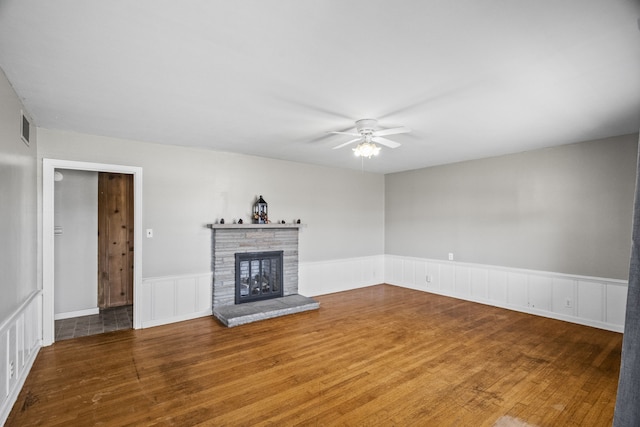 unfurnished living room with ceiling fan, a stone fireplace, and hardwood / wood-style floors